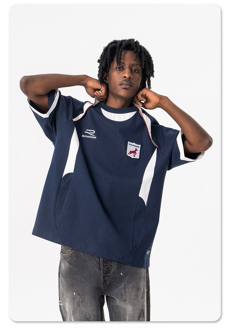 Oversized navy varsity football tee with white sleeve stripes and crest patch on model
