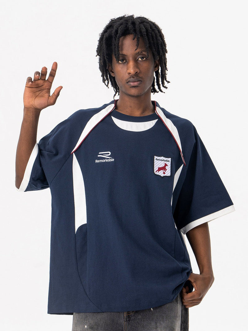 Oversized navy varsity football tee with white trim and crest logo, styled on a model against a white background