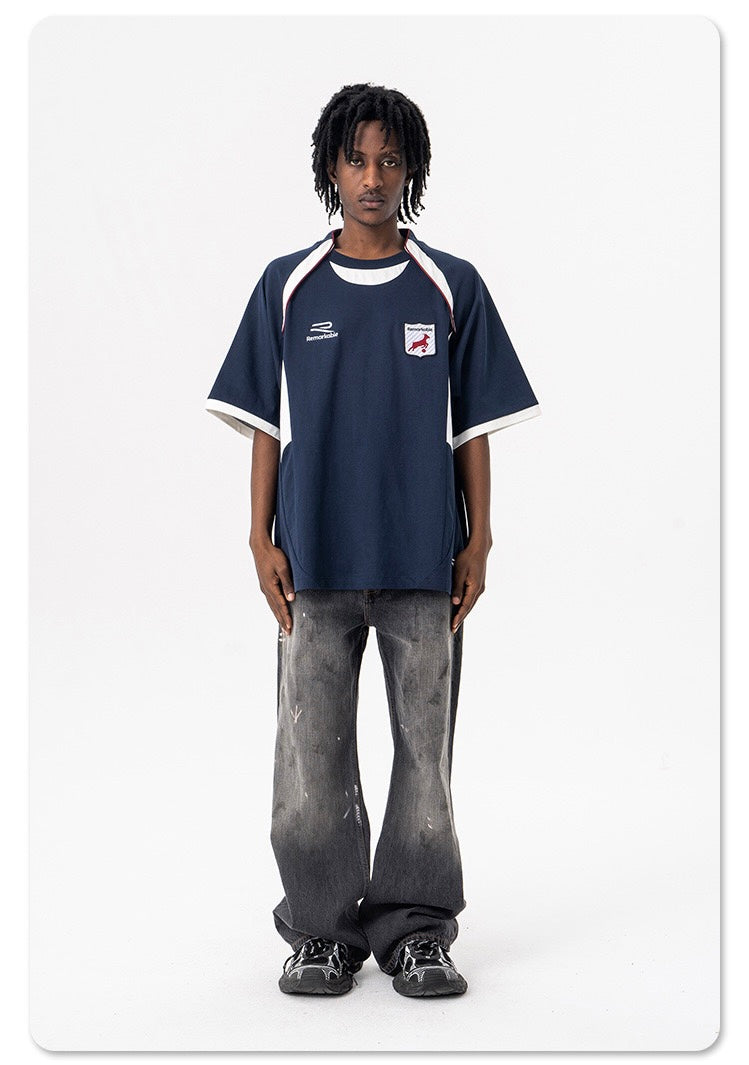 Oversized navy varsity football tee with crest patch, white trim, and relaxed short sleeves worn with faded jeans