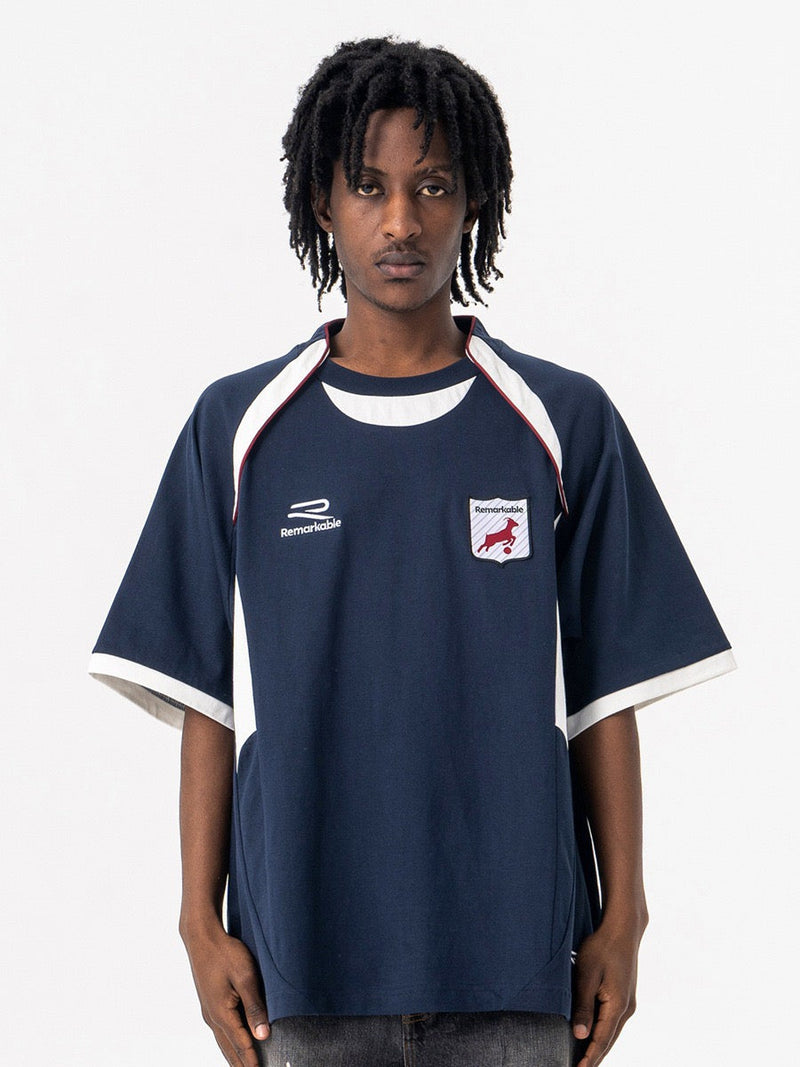 Oversized navy varsity football tee with white trim, chest crest, and raglan sleeves worn by a model