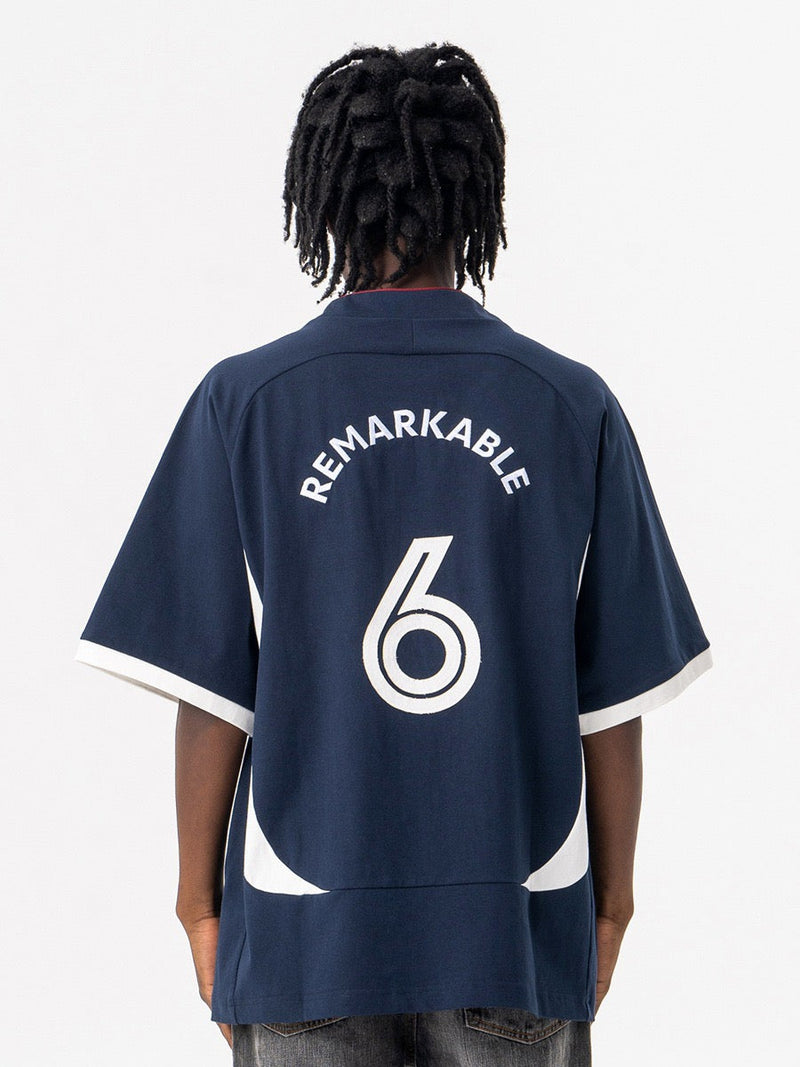 Oversized navy football jersey tee with REMARKABLE 6 print and white trim, shown from the back on a model