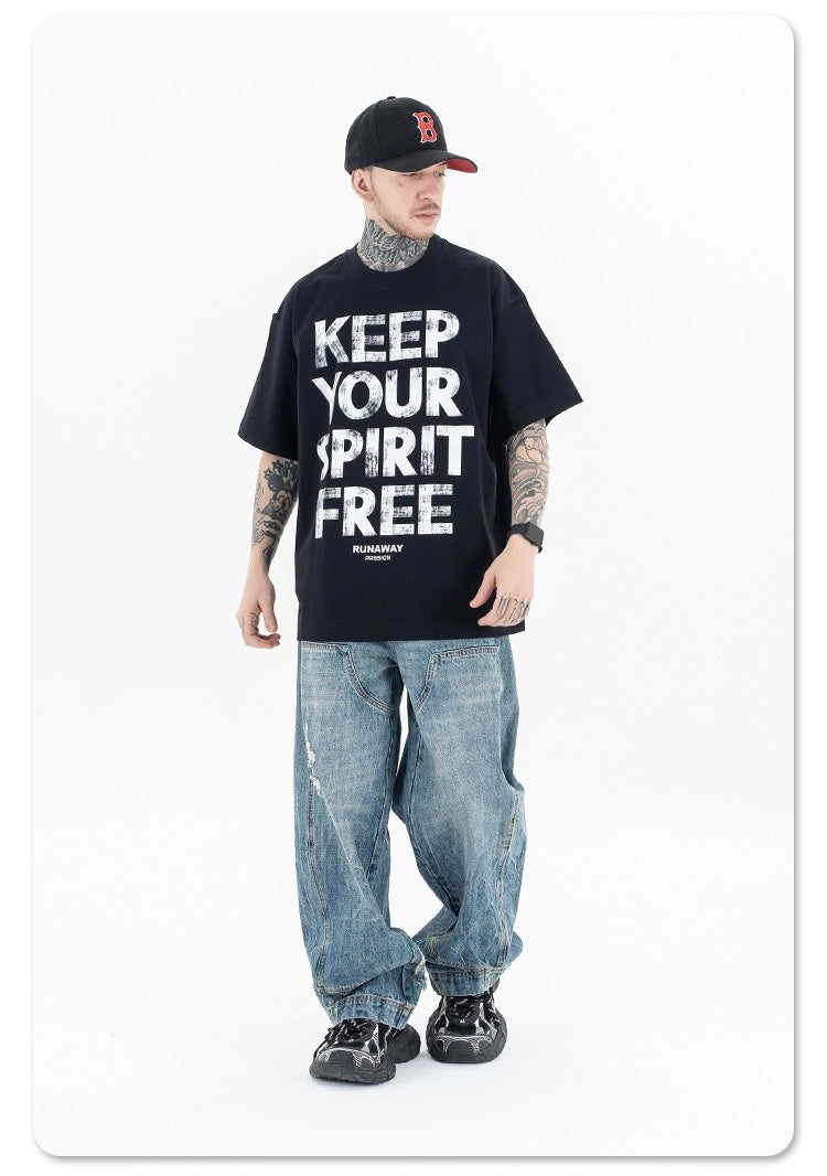 Model wearing black oversized graphic tee with bold Keep Your Spirit Free print, baggy jeans, and cap