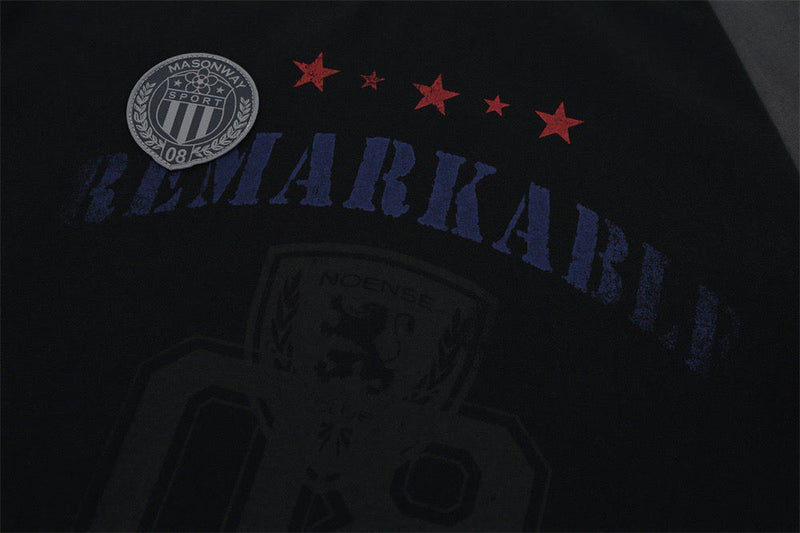 Black varsity tee with faded navy collegiate lettering, red stars, and a grey crest patch on the chest