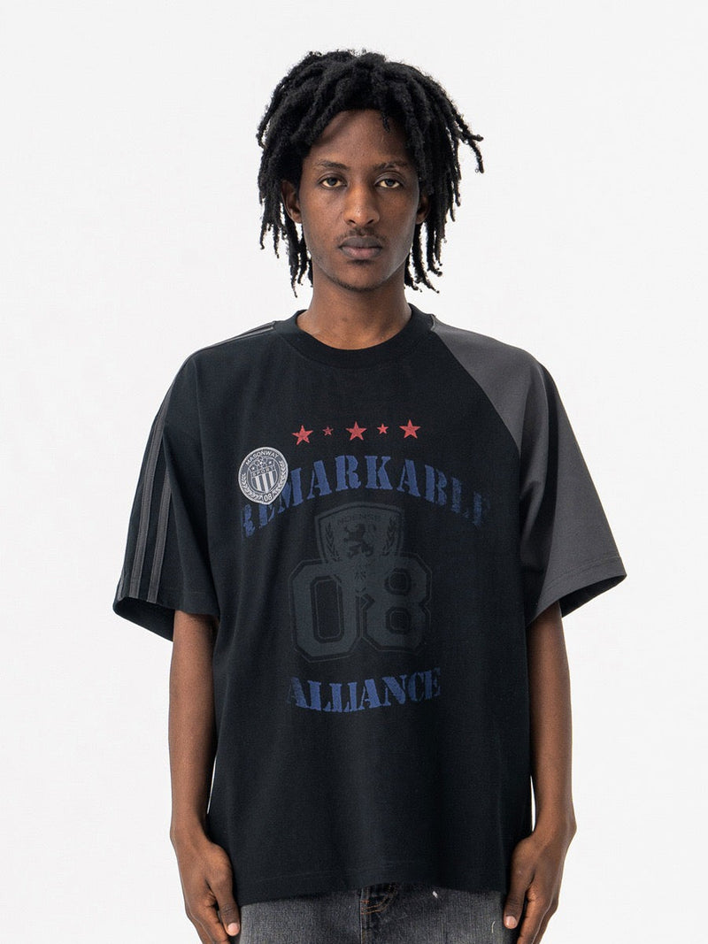 Black varsity tee with contrast shoulder panels and collegiate graphic print on the front, worn by a male model