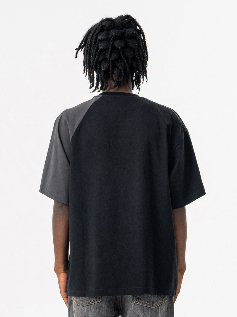 Black varsity tee with gray contrast raglan sleeves shown from the back on a model, collegiate streetwear style