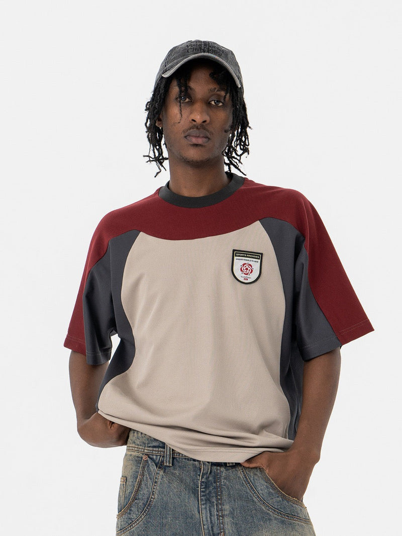 Oversized retro colorblock tee with burgundy, beige, and charcoal panels, worn with a black cap and jeans