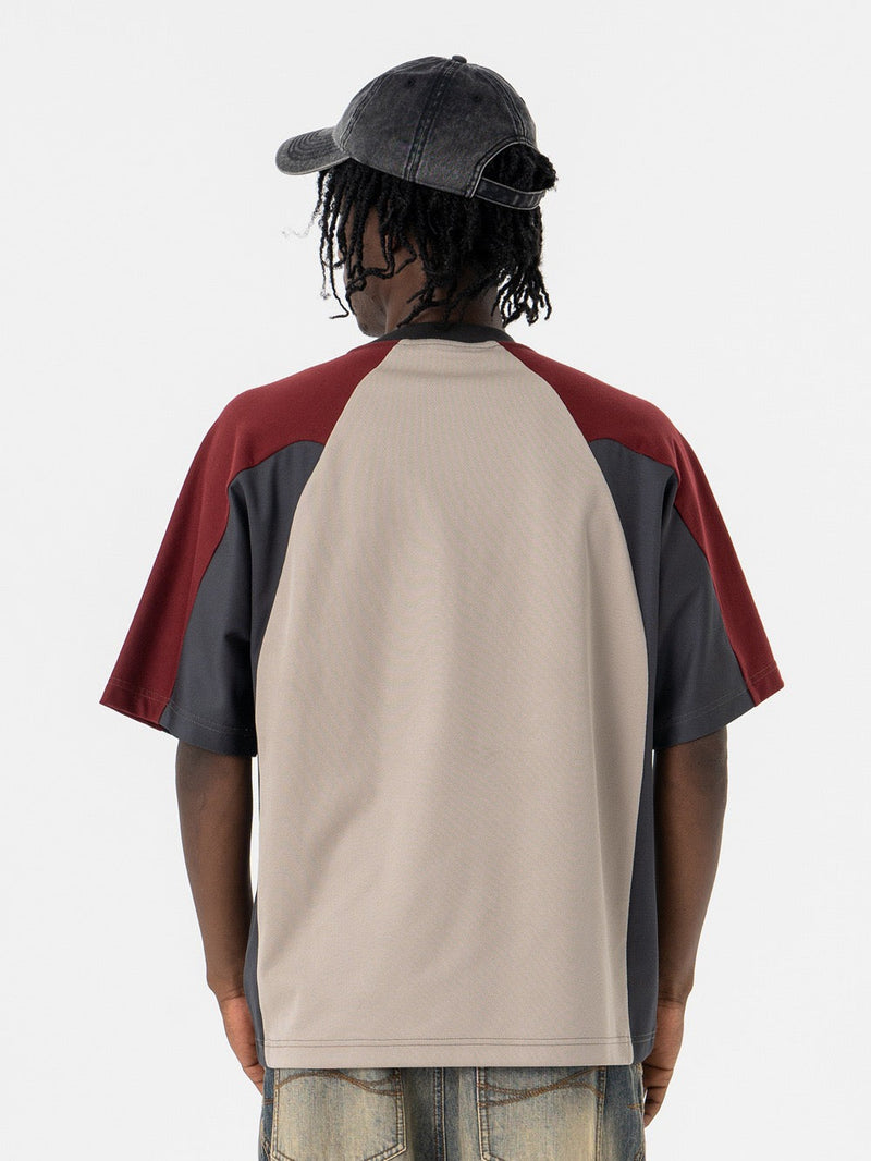 Oversized colorblock T-shirt with beige back panel, burgundy and charcoal sleeves, worn by model from behind