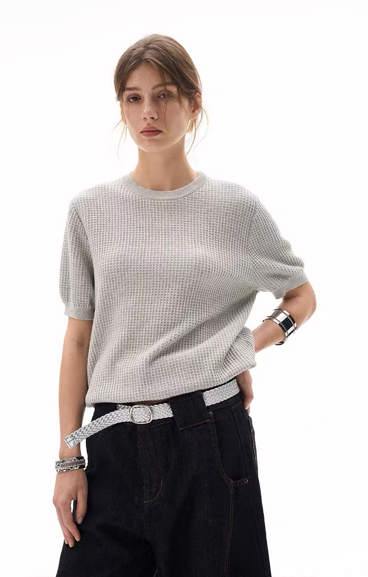 Model wearing a light gray waffle knit short-sleeve sweater with a relaxed fit and black jeans