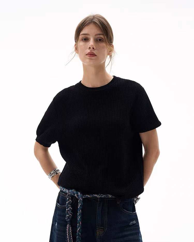 Black waffle knit short-sleeve sweater with relaxed fit, worn with jeans on a model against a white background