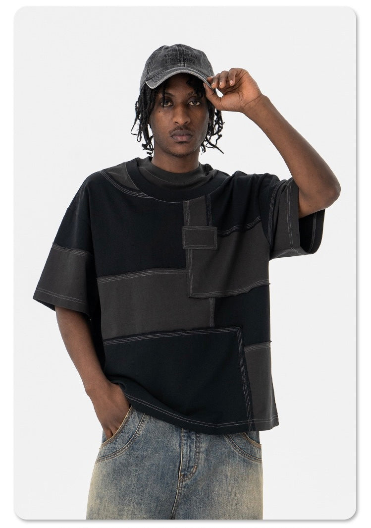 Model wearing oversized black patchwork panel T-shirt with contrasting seam details and distressed jeans