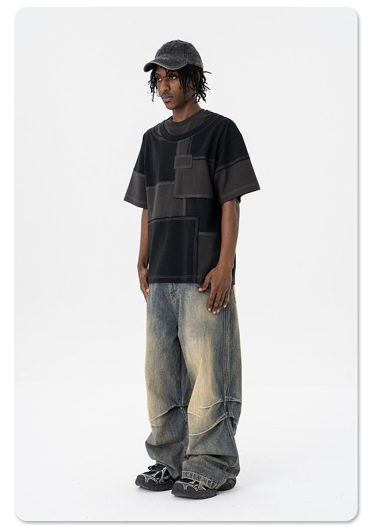 Model wearing an oversized black patchwork T-shirt with wide faded jeans and a black cap in a streetwear look