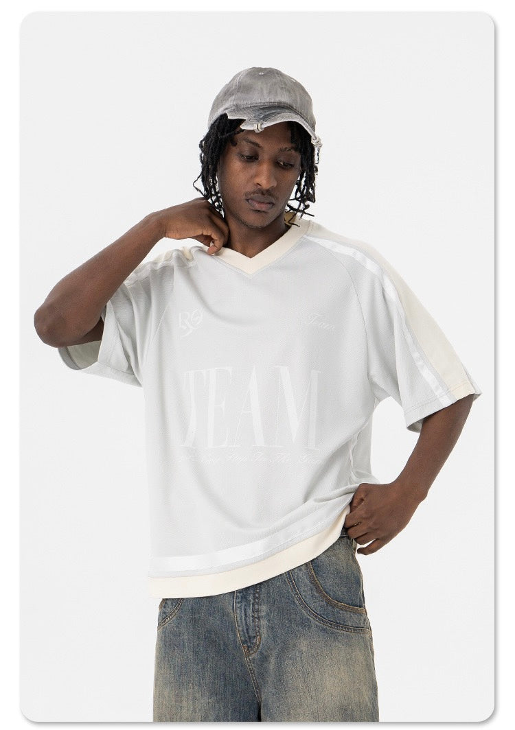 Oversized white mesh varsity tee with cream trim, worn by a model with denim jeans and a gray cap