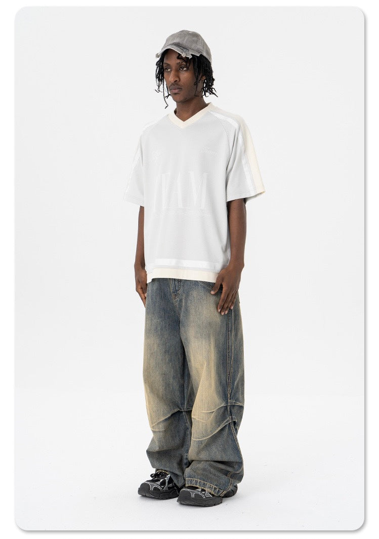 Oversized white mesh varsity tee worn with baggy faded jeans and black sneakers on a model standing against a white background