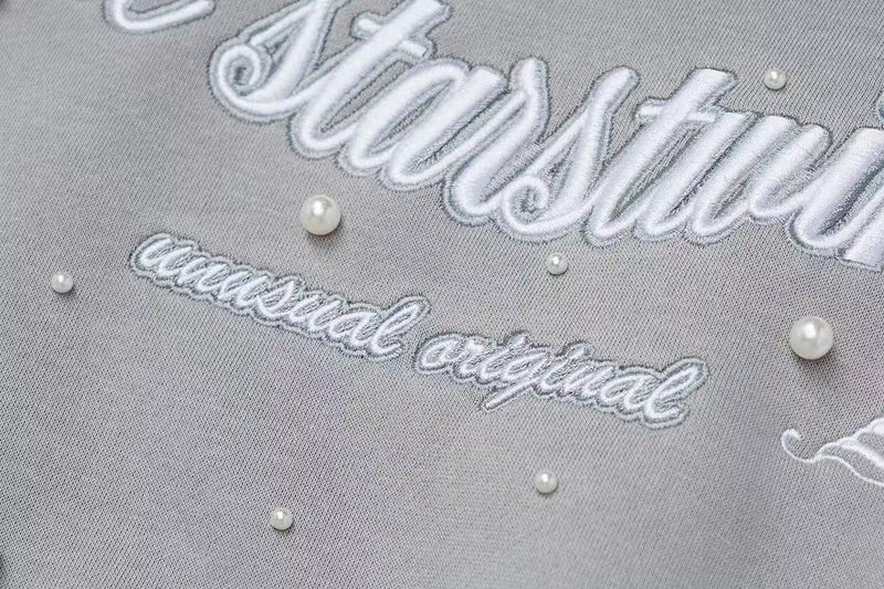 Close-up of gray hoodie embroidery reading The starstwinkle with small pearls
