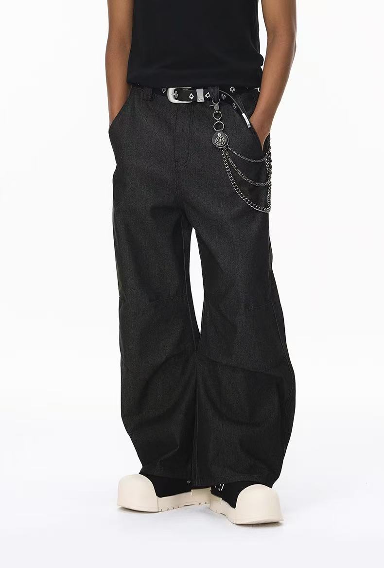 Close-up of black wide-leg pants with belt, chain detail, and cream shoes at the hem