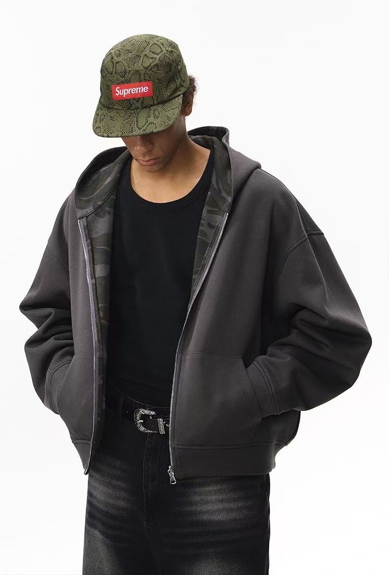 Model wearing solid charcoal side of reversible hoodie with camo hood lining