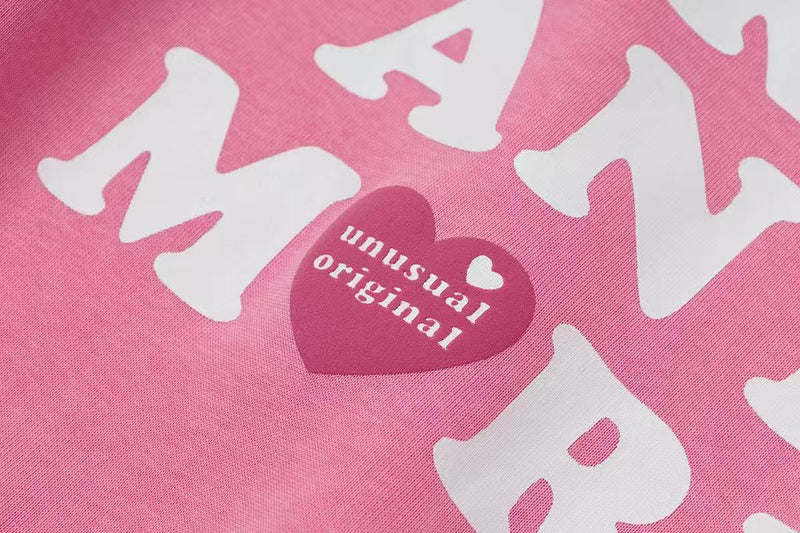 Close-up of pink hoodie graphic with white letters and a small heart reading unusual original