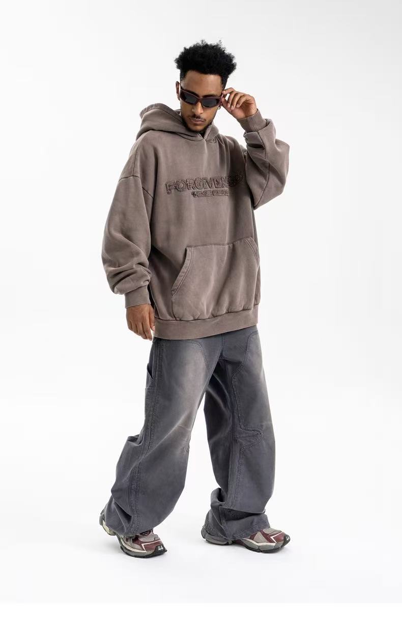Front angled view of brown-gray oversized hoodie with kangaroo pocket and embroidered chest text