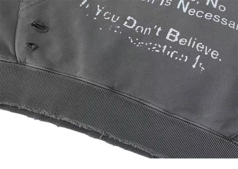 Close-up of gray hoodie hem with ribbed trim, printed text, and distressed holes
