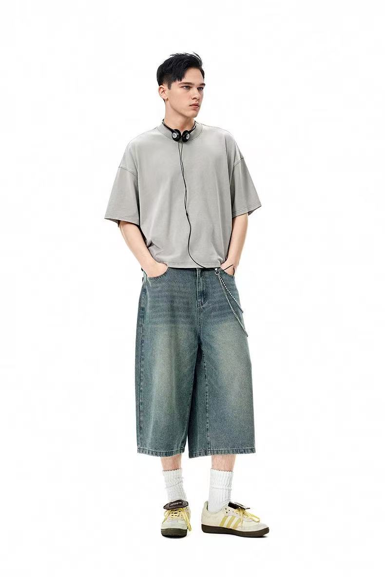 Model wearing an oversized washed gray tee with wide-leg denim shorts, white socks, and sneakers on a white background