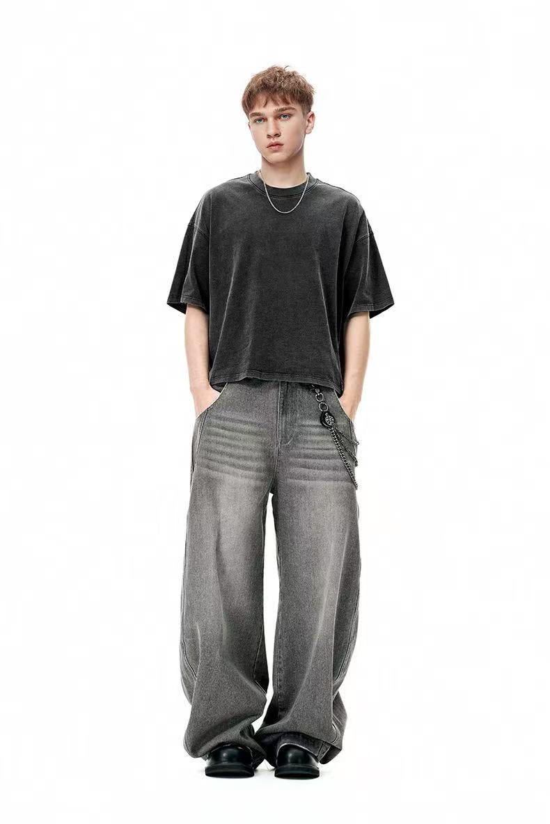 Oversized washed black heavyweight cotton tee worn with wide-leg gray jeans and chain detail on a studio model