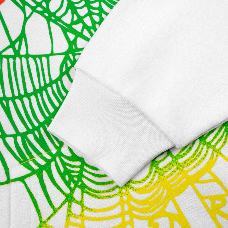 A close-up of a Sp5der “Toxic Web” Hoodie – White & Neon Lime, 440GSM heavyweight oversized streetwear pullover sleeve resting on fabric with an abstract green and yellow web-like pattern.
