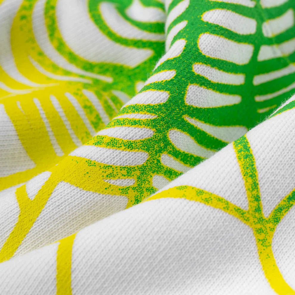 Close-up of Sp5der "Toxic Web" Hoodie—White & Neon Lime, 440GSM heavyweight cotton fleece with green and yellow abstract leaf-like patterns, highlighting texture and folds. Perfect for bold Y2K-inspired streetwear looks.