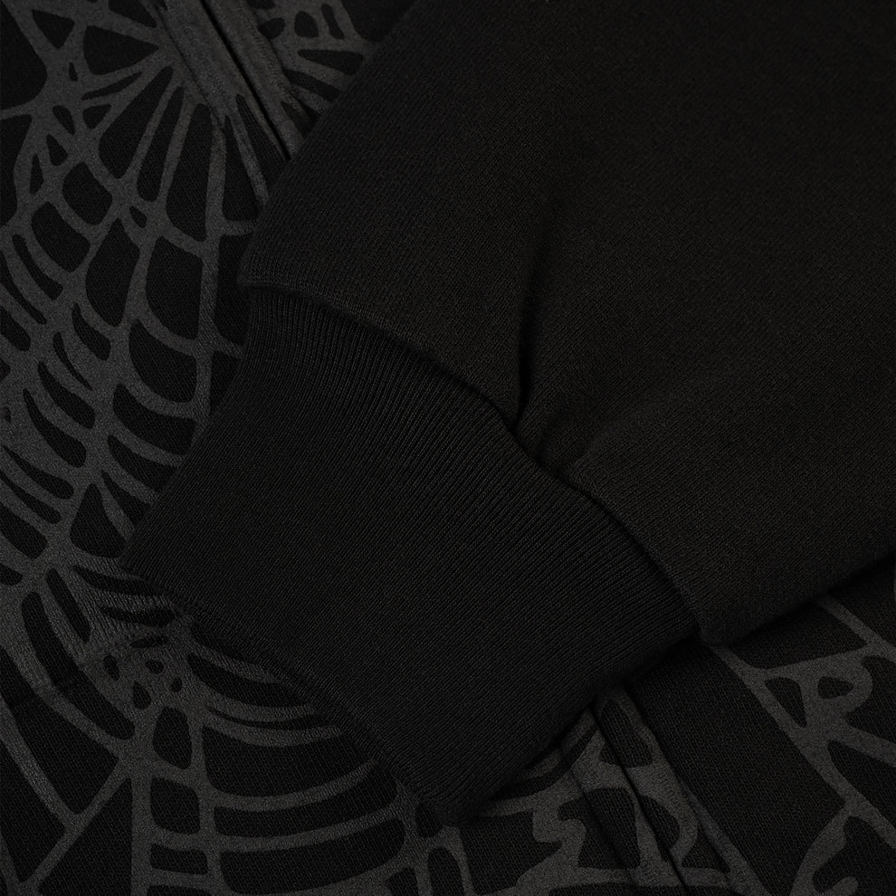 Close-up of the Sp5der Tonal Web Zip Hoodie – Black, a 440GSM heavyweight streetwear piece, showing its ribbed cuff sleeve resting on fabric with a subtle tonal spider web graphic.