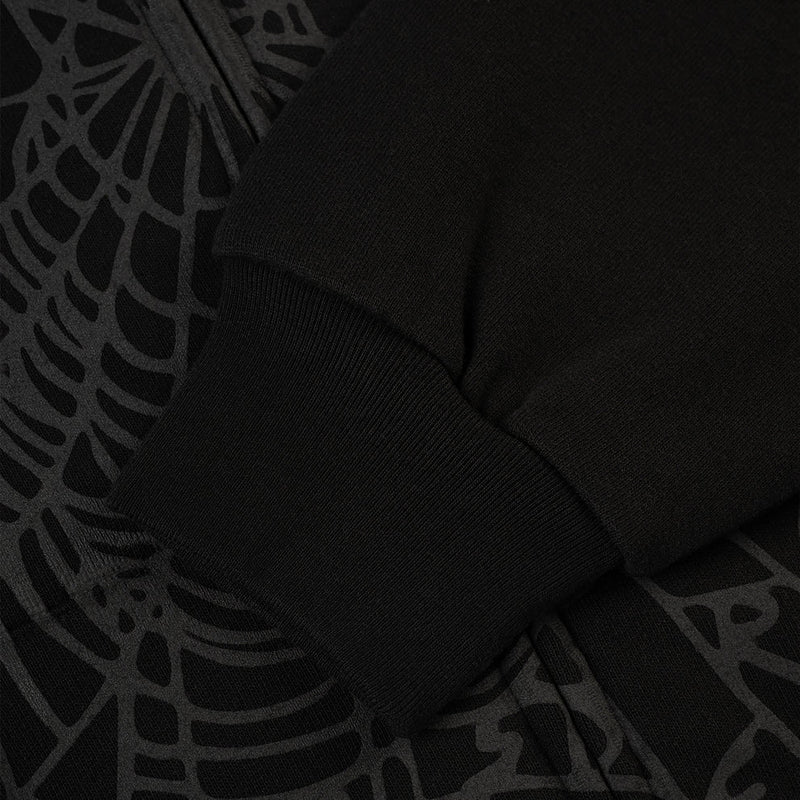 Close-up of the Sp5der Tonal Web Zip Hoodie – Black, a 440GSM heavyweight streetwear piece, showing its ribbed cuff sleeve resting on fabric with a subtle tonal spider web graphic.