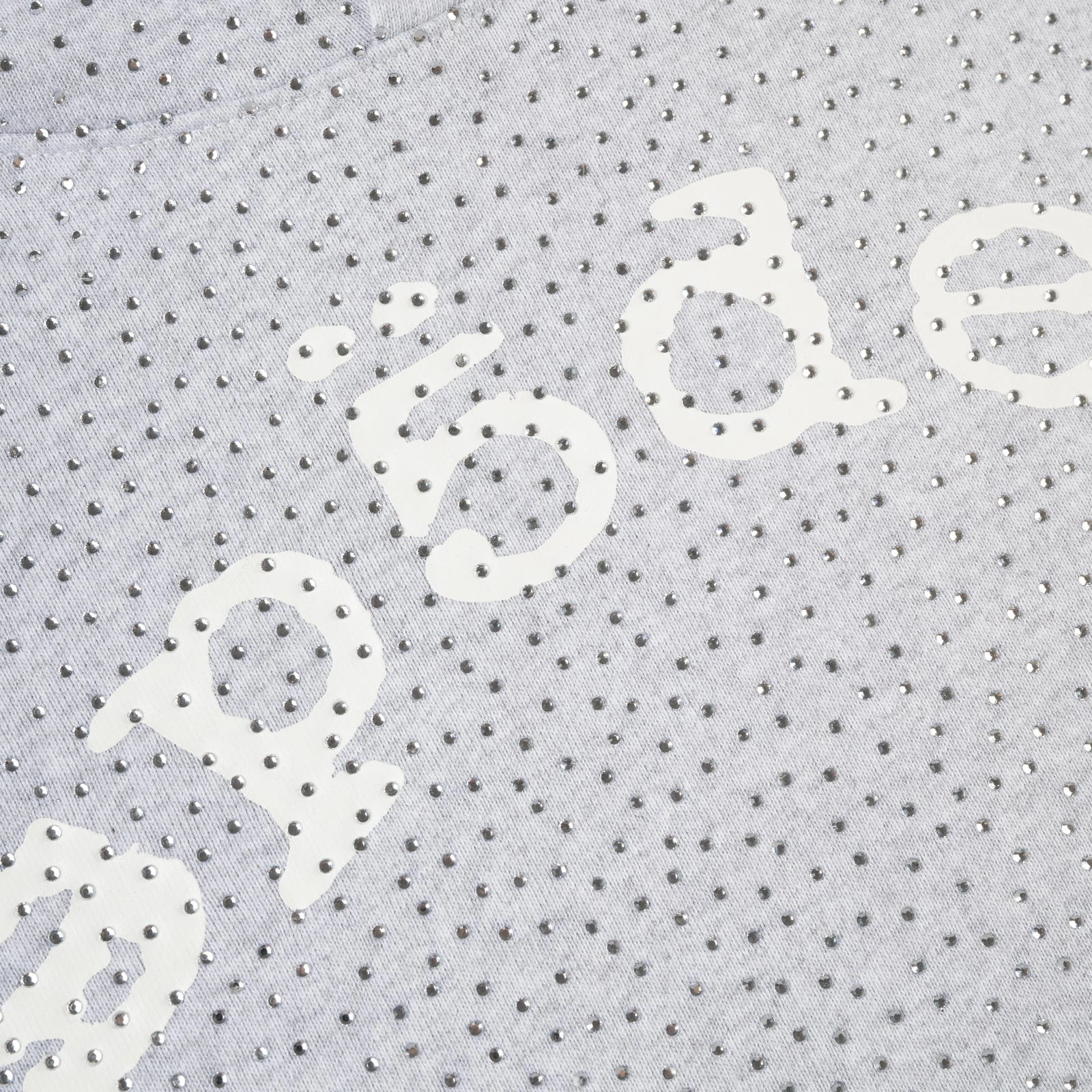 Close-up of the Grey Sp5der Rhinestone VVS Hoodie 440GSM, featuring light grey fabric embellished with all-over silver rhinestones and partially visible white curved lettering.