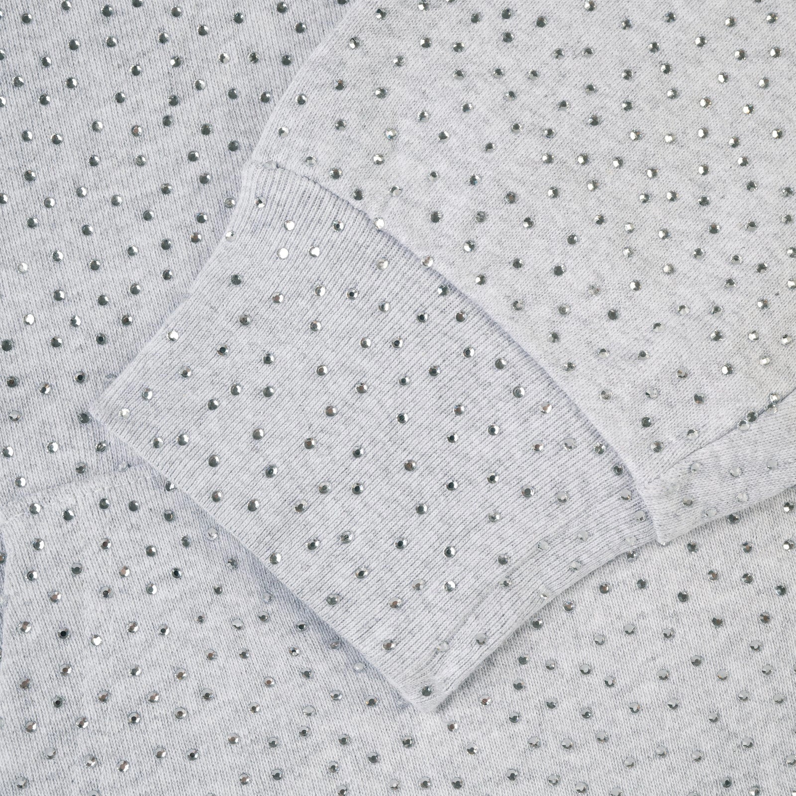 Close-up of the Grey Sp5der Rhinestone VVS Hoodie 440GSM, featuring light gray knit fabric with ribbed cuffs and evenly placed shiny silver rhinestones for a subtle, elegant pattern.