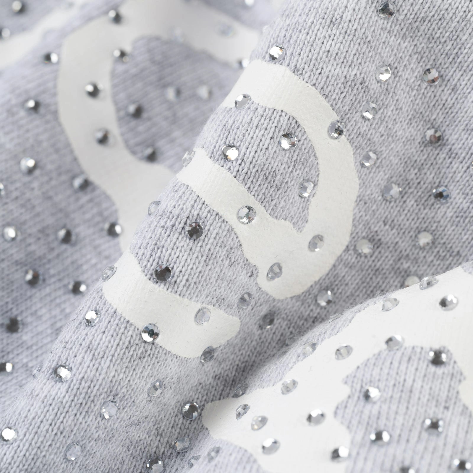 Close-up of the Grey Sp5der Rhinestone VVS Hoodie 440GSM, showing its light gray fabric with a white printed pattern and all-over shiny rhinestone embellishments on the textured, slightly wrinkled surface.