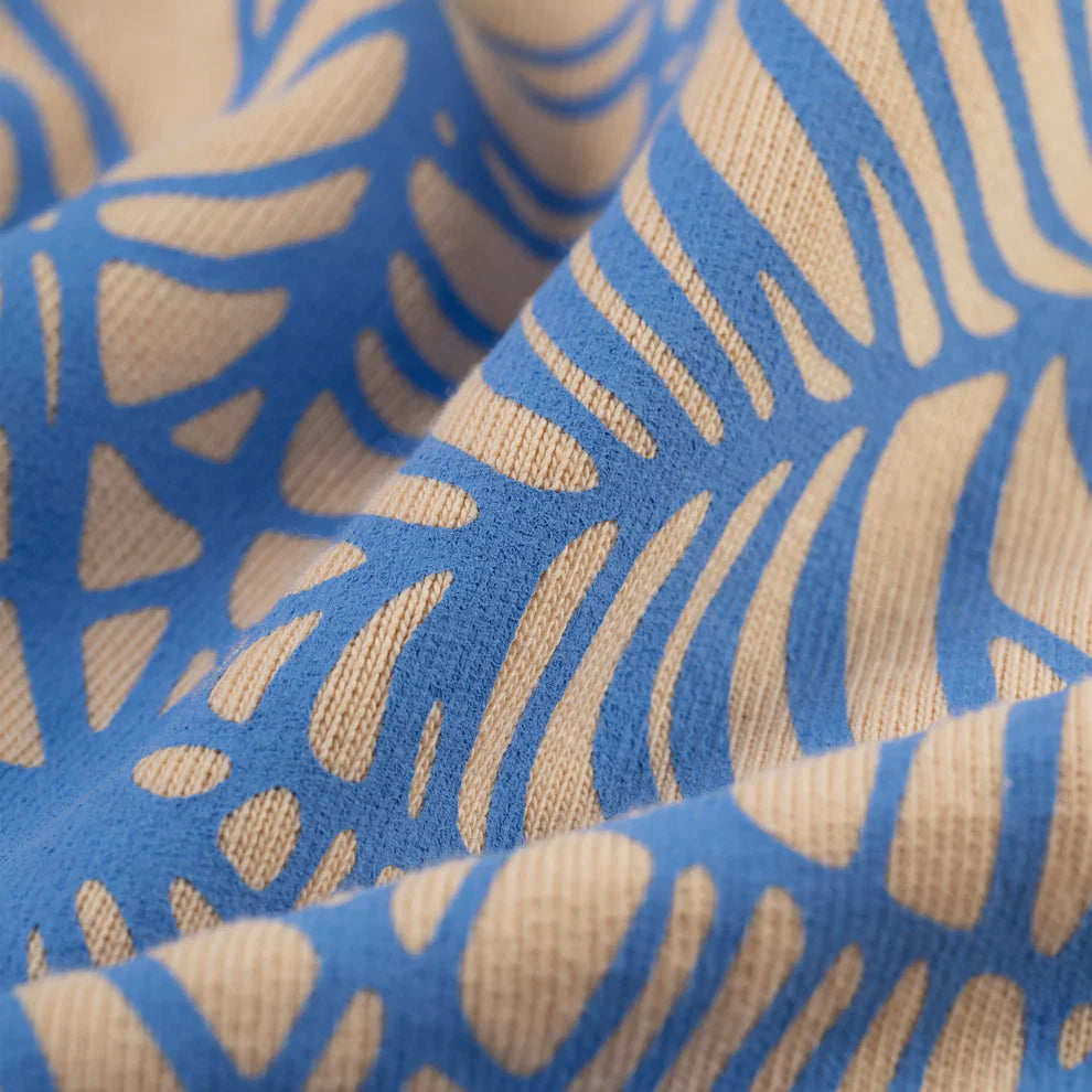 Close-up of the Sp5der “Sky Web” Hoodie’s cream heavyweight 440GSM cotton fleece, featuring a blue and green abstract leaf-like pattern. The slight wrinkles highlight its soft, textured Y2K-inspired oversized streetwear design.