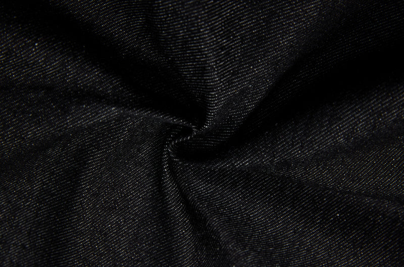Close-up of dark denim fabric gathered in folds, showing the woven texture