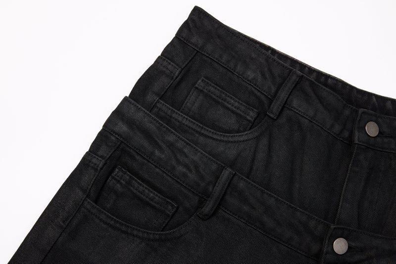 Close-up of black denim front pocket, waistband, and button on layered waist design
