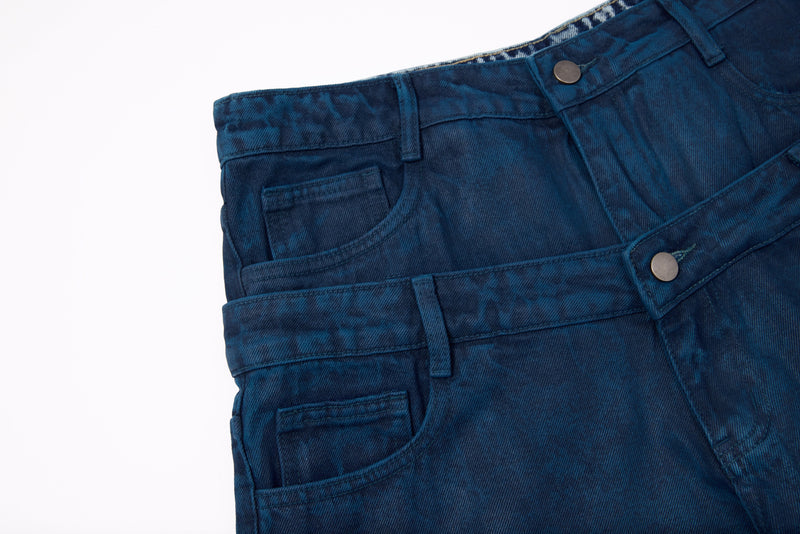 Close-up of overlapping front waist details on dark blue denim jeans