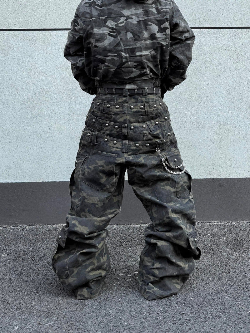 Model wearing camo wide-leg cargo pants with layered studded belt detail and loose legs
