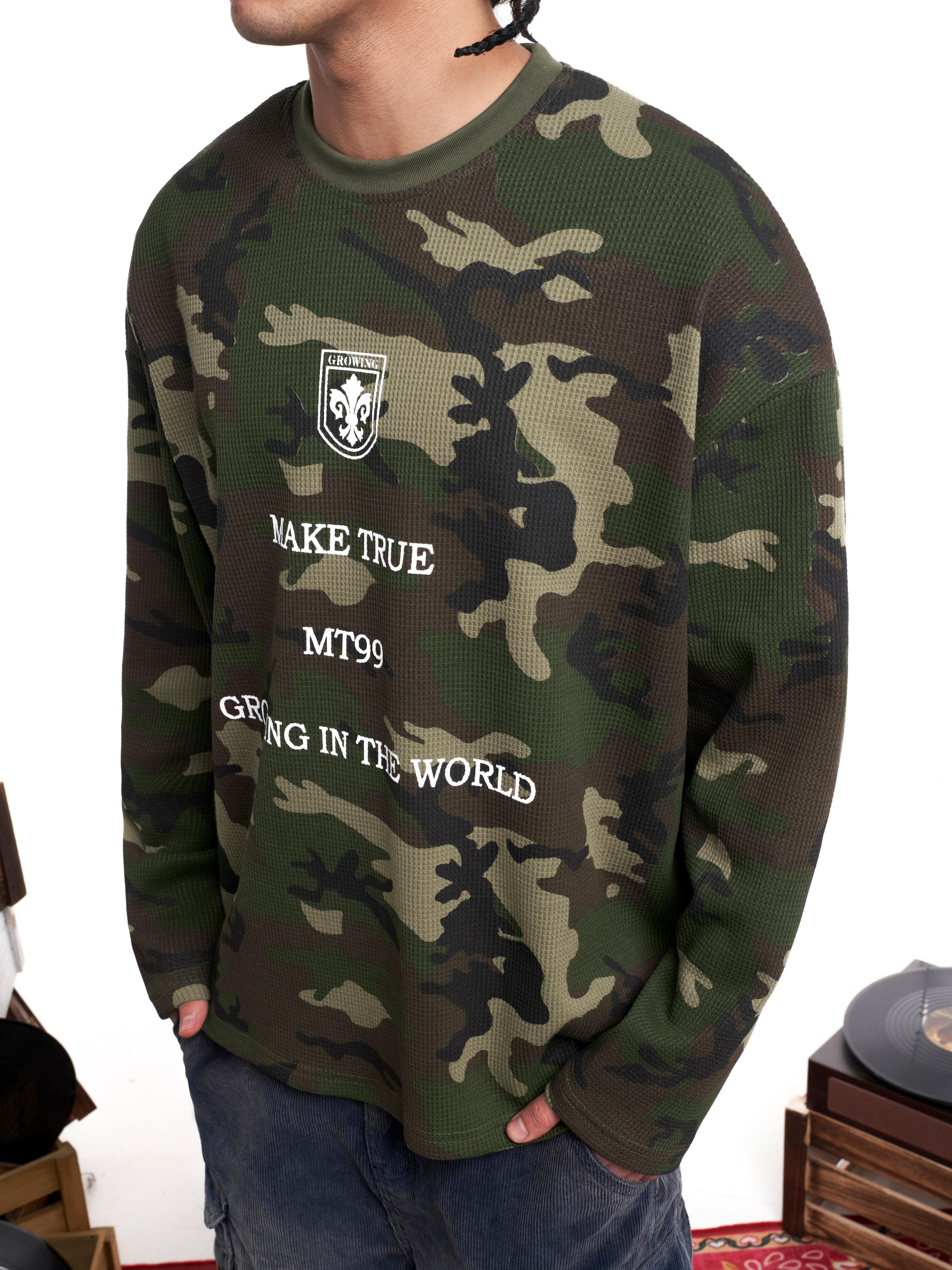 Man wearing an oversized woodland camo waffle-knit longsleeve with white text graphics on the front
