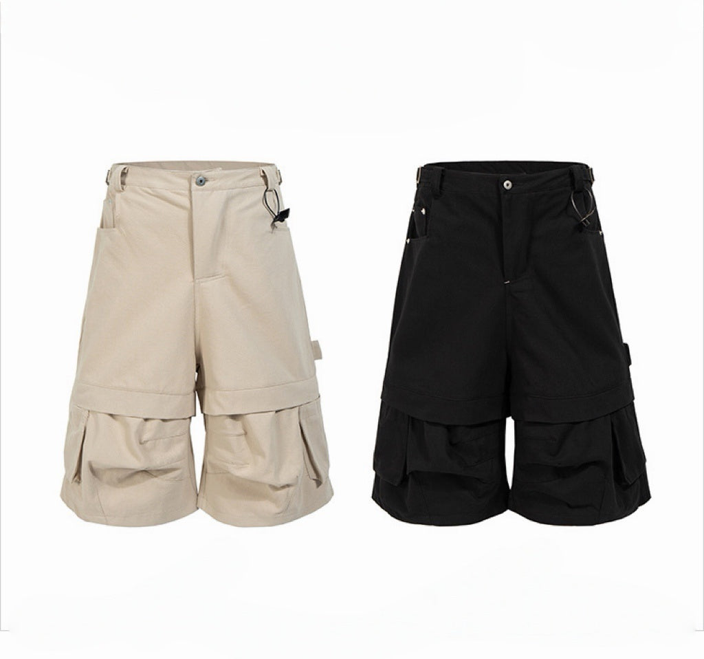 Black layered utility cargo shorts with oversized pleated pockets, D-ring hardware and double-panel construction, front view