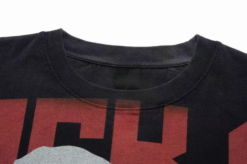 Close-up of a black oversized graphic tee with vintage wash, ribbed crew neck, and bold red printed lettering