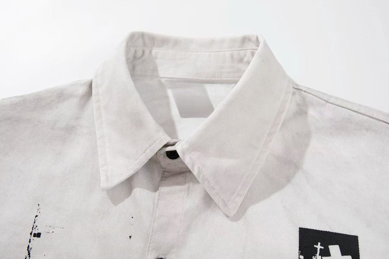 Light gray short sleeve shirt with pointed collar and distressed black graphic print on the chest