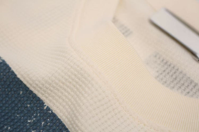 Close-up of cream waffle knit fabric with a blue textured panel and visible streetwear tee stitching
