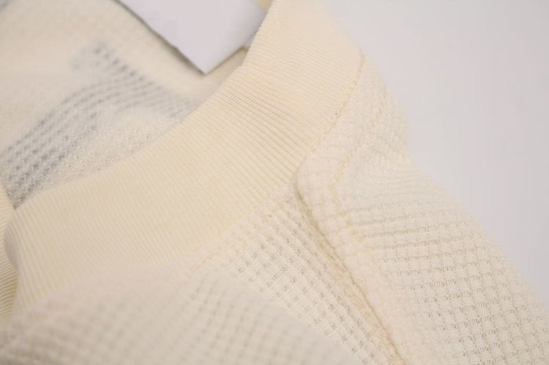 Cream waffle knit tee with close-up textured fabric and subtle streetwear graphic detail