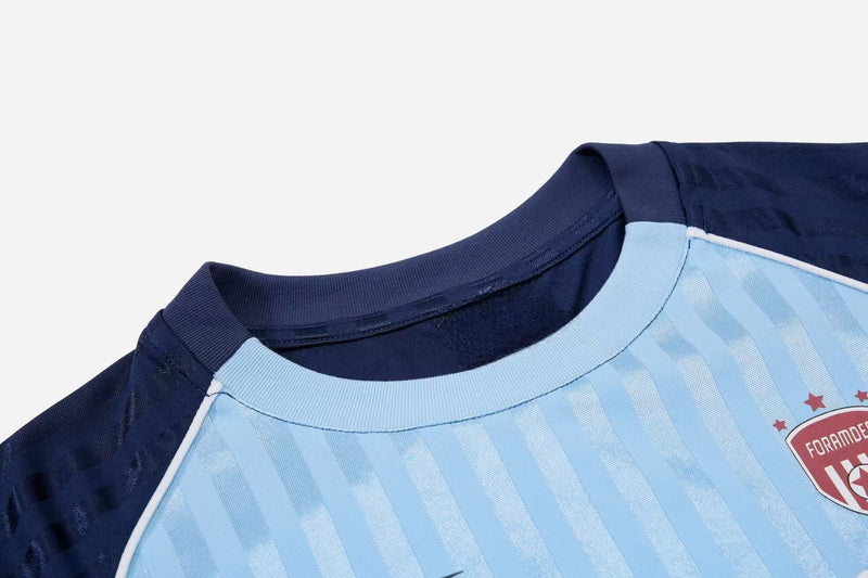 Light blue striped football jersey tee with navy collar and shoulders, featuring a crest on the chest