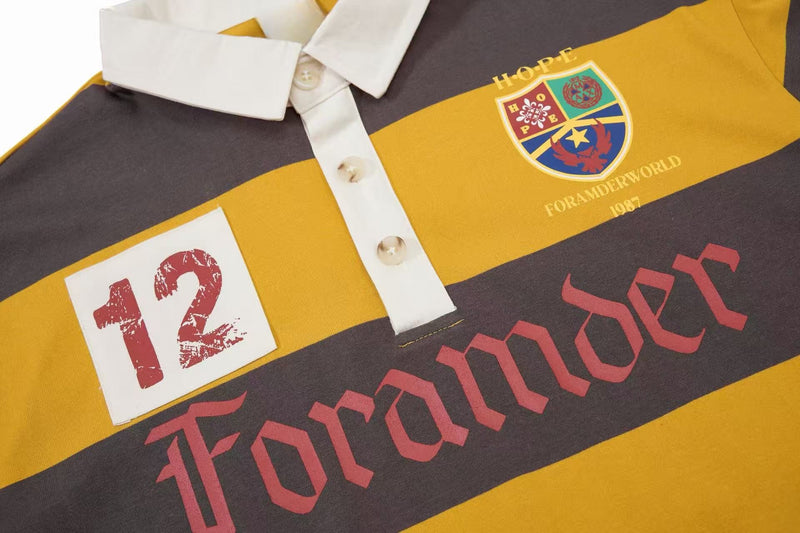 Close-up of a striped rugby polo shirt with white collar, button placket, crest patch, and bold vintage-style graphics