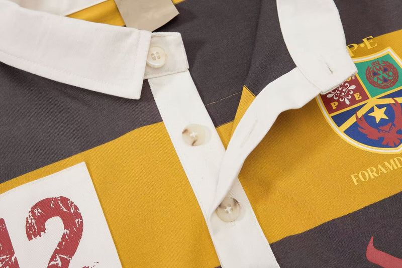 Close-up of a striped rugby polo with white collar, buttons, and colorful varsity-style crest patches