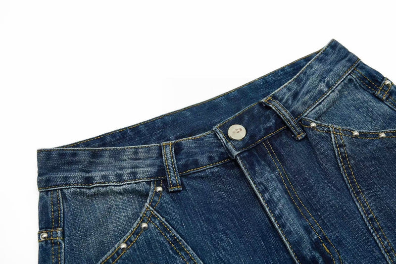 Close-up of blue denim waistband with button, belt loops, and studded seam details