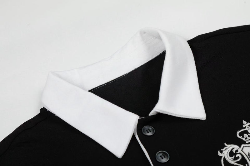 Black polo shirt with white contrast collar, button placket, and embroidered crest detail on the chest