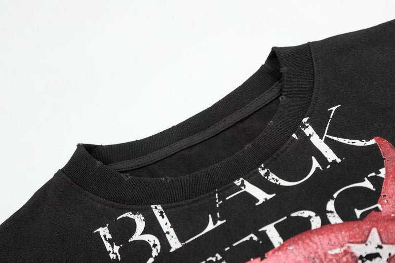 Black graphic tee with distressed white lettering and red devil lip print on the chest, shown on a plain white background