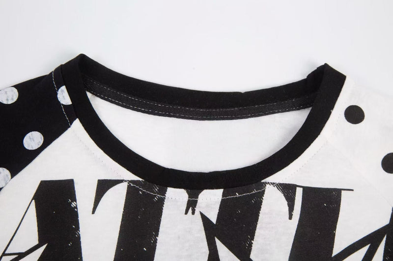 Close-up of black ribbed crew neckline on white raglan tee with polka dot sleeves